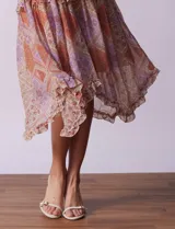 Vestido midi de gasa estampada con motivos geométricos en tonos naranja, lila y beige. Tiene breteles finos regulables, escote en V con volados y falda asimétrica con volados.