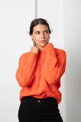 Buzo de lana color coral con diseño de tejido trenzado, cuello redondo y mangas largas.