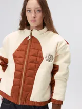 Campera crop de corderito color marfil, con parches capitoneados en contraste color tostado en el pecho y las mangas. Cuenta con cuello alto, cierre frontal metalizado, puños y bajo elásticos, y logo bordado en el pecho.