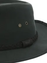 Sombrero tipo fedora de color verde oscuro, confeccionado en canvas engrasado resistente al agua. Presenta una banda decorativa trenzada en tono oscuro y ojales metálicos laterales para ventilación.