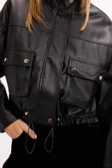 Campera corta de cuero sintético en color beige, con diseño de calce relajado, cierre frontal metálico, bolsillos con solapa en el frente y cordón ajustable en el ruedo.