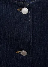Chaqueta corta de denim color azul oscuro, con cuello redondo, cierre frontal de botones y dos bolsillos de parche delanteros.