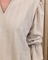 Blusa blanca de algodón con escote en V y cuello mao. Presenta mangas largas abullonadas con puños acampanados y fruncidos.