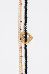 Collar de diseño multicapa compuesto por una tira de cuentas de cristal negro con un dije central en forma de corazón dorado, una fina cadena dorada con pedrería y otra cadena dorada decorada con pequeñas cuentas de colores.