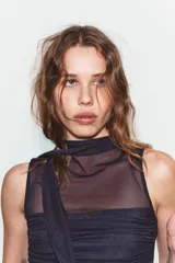 Top sin mangas confeccionado en tul semitransparente, con cuello drapeado y detalle de tira larga tipo foulard. Presenta frunces laterales y diseño ajustado.