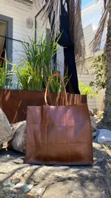 Bolso tote grande de cuero natural en color marrón, con diseño de piezas unidas mediante costuras visibles y asas de hombro.
