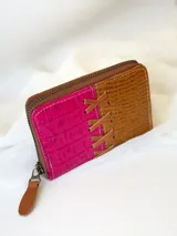 Billetera pequeña de cuero color fucsia y marrón con textura tipo piel de cocodrilo. Tiene cierre metálico y detalle de tiras de cuero cruzadas en el frente.