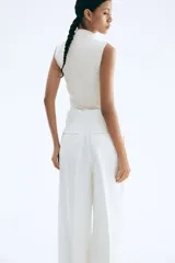 Top sin mangas color blanco hueso, de tejido liso y corte ajustado, con cuello alto tipo mock neck y bordes sin rematar.