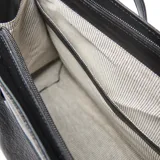 Cartera shopper de cuero negro con textura granulada, doble asa de hombro y detalles de tiras con hebillas metálicas. Cuenta con el logo de la marca en aplique metálico frontal.