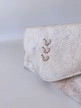 Billetera de cuero con textura rústica y acabado desgastado, presenta un diseño de solapa triangular con un detalle bordado en forma de espiga en el centro.