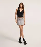 Mini pollera de jeans de tiro bajo, color gris claro, con cintura traspasada y cierre de botón. Presenta trabillas para cinturón y bolsillos delanteros y traseros.