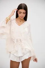 Blusa color crudo con volados en el frente y en las mangas largas, confeccionada en tela semitransparente con cierre frontal de botones.