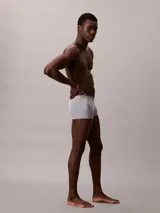 Pack de tres boxers tipo trunk de Calvin Klein confeccionados en microfibra elástica suave. Presentan un diseño de talle bajo con cinturilla elástica distintiva de la marca sin costuras y bolsillo frontal con soporte. El conjunto incluye colores gris claro, azul marino y turquesa.