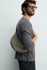 Bolso de hombro de nylon color negro, con diseño curvo y cierre de cremallera en el compartimento principal. Cuenta con asa ajustable para llevar al hombro y bolsillo interior con cierre.