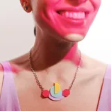 Collar con cadena plateada y dije geométrico con formas circulares y hexagonales en colores pastel: amarillo, celeste, lila y rosado.