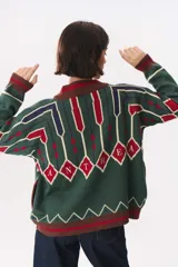 Campera tipo bomber tejida con diseño jacquard geométrico en tonos azul marino, blanco, rojo y verde. Presenta cierre frontal completo, cuello, puños y ruedo acanalados en color verde y blanco, con corte oversized y hombros caídos.