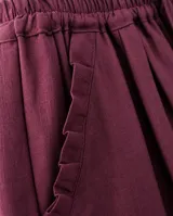 Pantalón de lino color bordó, con silueta relajada, cintura elastizada con lazo de ajuste, bolsillos laterales y detalle de pliegues con ruedo desflecado en los tobillos.