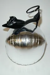 Zapatos de tacón tipo pump en terciopelo negro, con punta fina y un lazo grande decorativo en el empeine. Presentan una pulsera ajustable al tobillo con cierre de hebilla y tacón fino forrado.