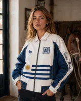 Campera de jean de corte recto y calce relajado, confeccionada en denim de algodón. Combina tonos crudo y azul con bordados exclusivos de Sierra Mora, un caballo, las iniciales AM y detalles inspirados en la bandera uruguaya.