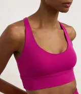 Top deportivo alargado color fucsia, con escote en U y cintura ancha. Posee tiras finas cruzadas en la espalda y copas removibles.