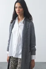 Cardigan de tejido de punto gris, con silueta larga, frente abierto, solapas clásicas y bolsillos aplicados en los laterales.