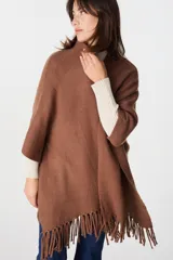 Ruana de tejido suave y envolvente en color blanco, con diseño de corte amplio y terminación de flecos en el ruedo.