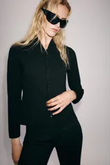 Chaqueta de punto negro con escote en V y manga larga. Cierre frontal con una hilera de pequeños botones forrados.