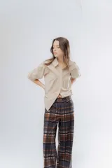 Pantalón de corte recto con diseño de cuadros escoceses en tonos marrones, negros y grises. Presenta una cintura elástica y una textura acanalada.