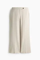Pantalón tobillero de corte bootcut, color beige, con cintura estándar, raya marcada al frente y en la espalda, y cierre con pretina prolongada y botón.