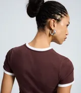 Remera de algodón color bordó con cuello redondo y bordes de mangas en color blanco. Presenta un diseño de estilo deportivo con estampado frontal que incluye el texto 'LATINA' y detalles de rayas blancas en los hombros.