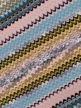 Capa o poncho de tejido de punto con diseño de zigzag multicolor, con cuello en V y flecos largos en el borde inferior.