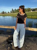 Remera negra de algodón con cuello redondo y mangas cortas. Presenta flores de crochet en tonos beige y blanco en el contorno del cuello y las mangas.