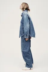 Campera camisera en denim rígido con cuello, cierre frontal de botones, puños abotonados, bolsillos de parche delanteros y dobladillo redondeado.