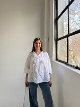 Camisa blanca de corte holgado y manga larga, con delicados bordados florales en tono gris claro en el frente.