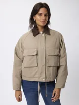 Campera corta de algodón en color beige, con cuello camisero en contraste color marrón, cierre frontal con botones a presión y dos bolsillos frontales tipo cargo.