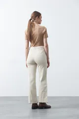 Pantalón de fit recto color beige, confeccionado en cotton spandex. Presenta costuras visibles y bordados decorativos en tono dorado/marrón claro. El ruedo del pantalón tiene un borde festoneado.