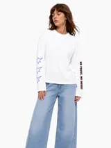 Remera de manga larga blanca con cuello redondo, corte holgado y estampados en las mangas: estrellas azules en la manga derecha y texto negro en la izquierda.