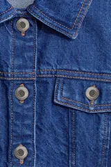 Chaleco de denim azul rígido de algodón, con cuello camisero, cierre frontal de botones metálicos, bolsillos con solapa en el pecho y detalle de peplum en la parte inferior.