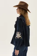 Blusa azul marino de algodón con volados en los hombros, mangas largas abullonadas y detalles de bordados florales y geométricos en el pecho y las mangas.