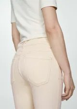 Jeans estilo flare color beige, confeccionados en tejido elástico de algodón. Presentan diseño crop, tiro alto, cinco bolsillos, trabillas para cinturón y cierre frontal con cremallera y botón. Los dobladillos tienen terminación deshilachada.