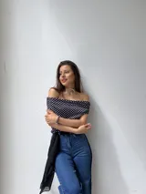 Top de escote bote y hombros descubiertos, confeccionado en tela elastizada con estampado de lunares blancos sobre fondo negro.