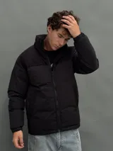 Campera puffer negra con diseño de paneles, cierre frontal completo y cuello alto. Presenta una textura diferenciada en la parte superior y bolsillos laterales.