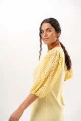 Vestido largo amarillo mantequilla con escote en V, mangas abullonadas y volados en el bajo con detalles de broderie.