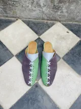 Zapatos tipo mule de punta cerrada y talón abierto, con diseño bicolor en tonos dorado y mostaza, con detalles cruzados en el empeine y suela baja.
