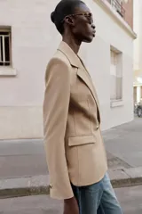 Blazer cruzado color beige, de manga larga, con cuello solapa y forro interior negro. Presenta cierre frontal con botones dorados y bolsillos de vivo en el pecho y bolsillos con solapa en el delantero.