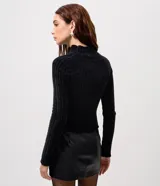 Blusa cropped de punto chenille color negro, con cuello alto y mangas largas raglán. Presenta una textura acanalada y pequeños puntos brillantes aplicados en el frente.