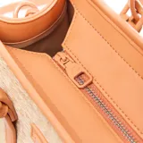 Cartera mediana tipo tote de diseño estructurado, confeccionada en material símil rafia con detalles en cuero sintético color tostado. Cuenta con doble asa de mano, correas decorativas frontales con hebillas, tira ajustable extraíble para el hombro y placa metálica con el logo de la marca.