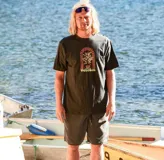 Remera Volcom de manga corta y cuello redondo en color negro, con estampado gráfico central que representa una planta con hojas en forma de ojos dentro de un arco decorativo y el logotipo de la marca.
