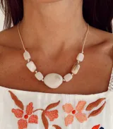 Collar de diseño artesanal compuesto por piedras irregulares en tonos crudos veteados, con una pieza central de mayor tamaño. Presenta un cordón beige ajustable y detalles en tono dorado.