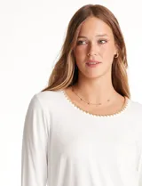 Remera de modal color blanco, con cuello redondo y mangas 3/4. Presenta un aplique bordado en color tostado en el cuello, los puños y el ruedo.